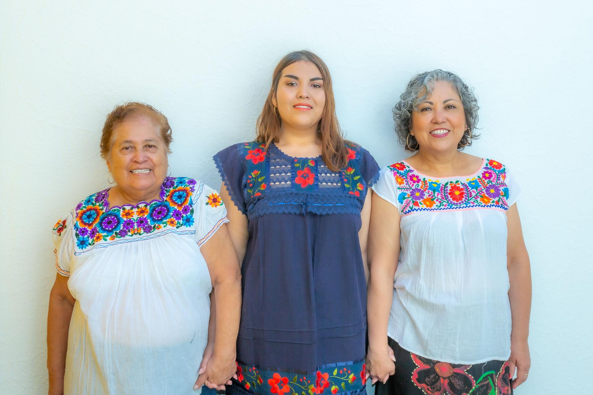 Three generations of latin Mexican women smiling, grandmother, granddaughter and daughter with floral printed blouses