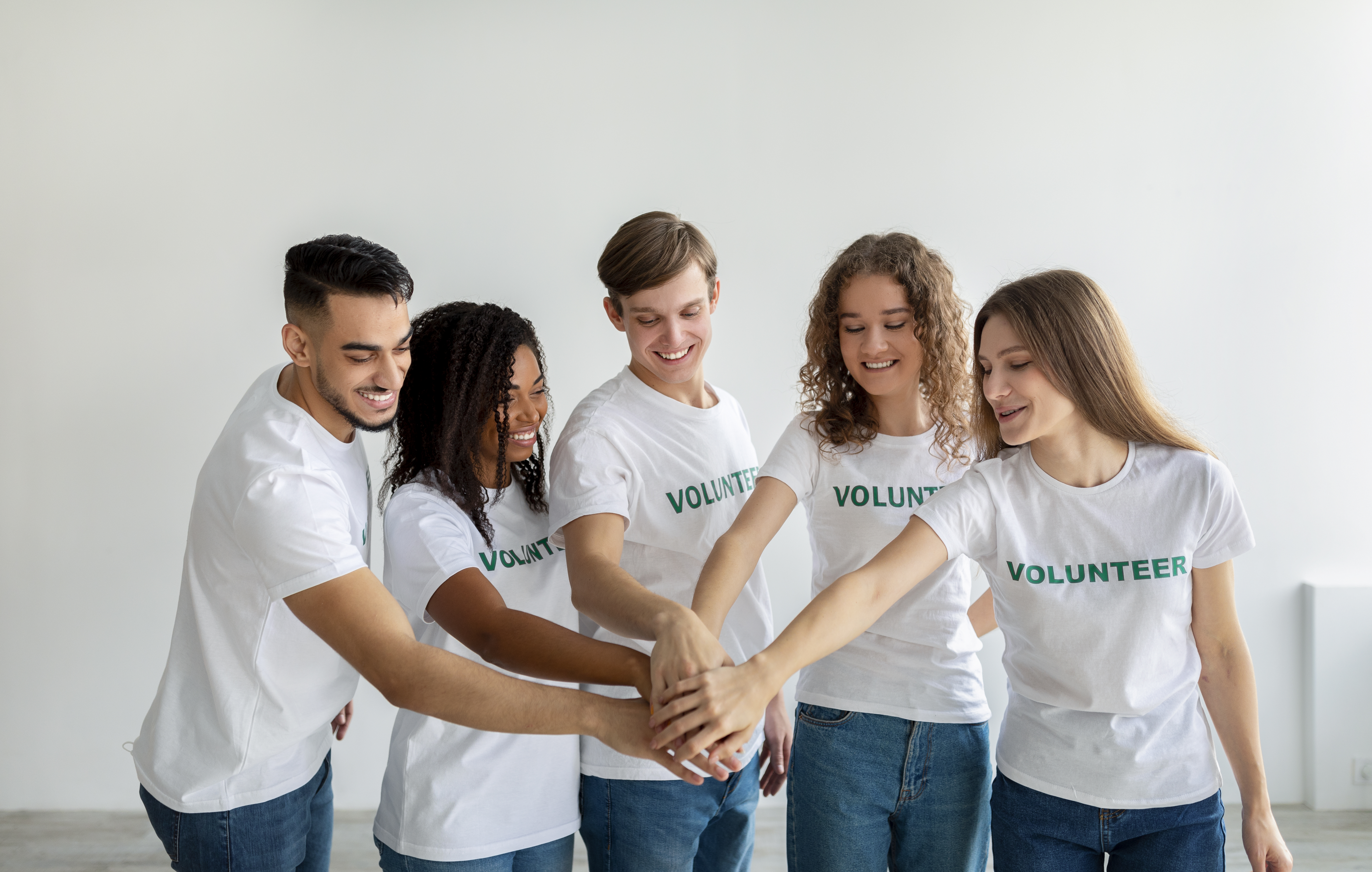 Mixed race young volunteers joining hands together and smiling, ready for work in charity organization center